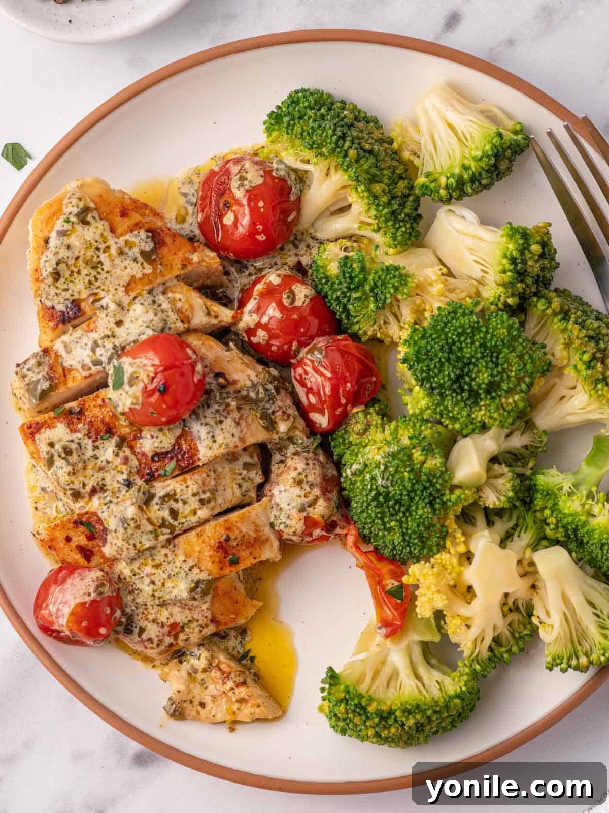 A plate featuring slices of creamy pesto chicken, alongside tender steamed broccoli florets, creating a balanced and appetizing meal.