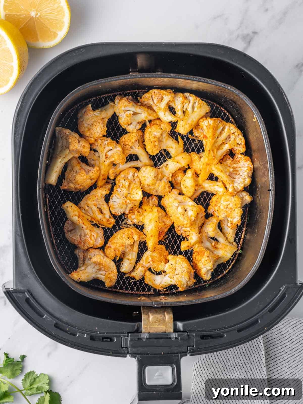 Seasoned and cheese-coated cauliflower florets laid out in a single layer inside an air fryer basket, ready for cooking.