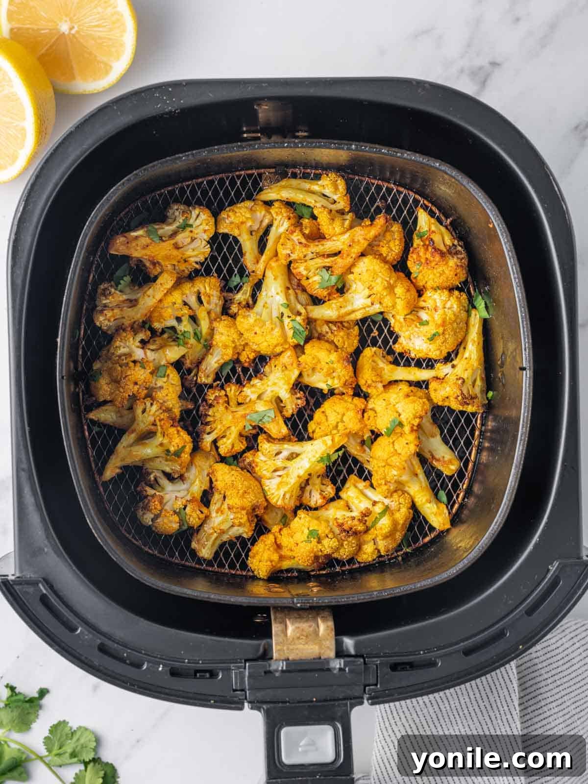 A close-up shot of golden-brown and crispy roasted cauliflower florets piled in an air fryer basket, freshly cooked and ready to be served.