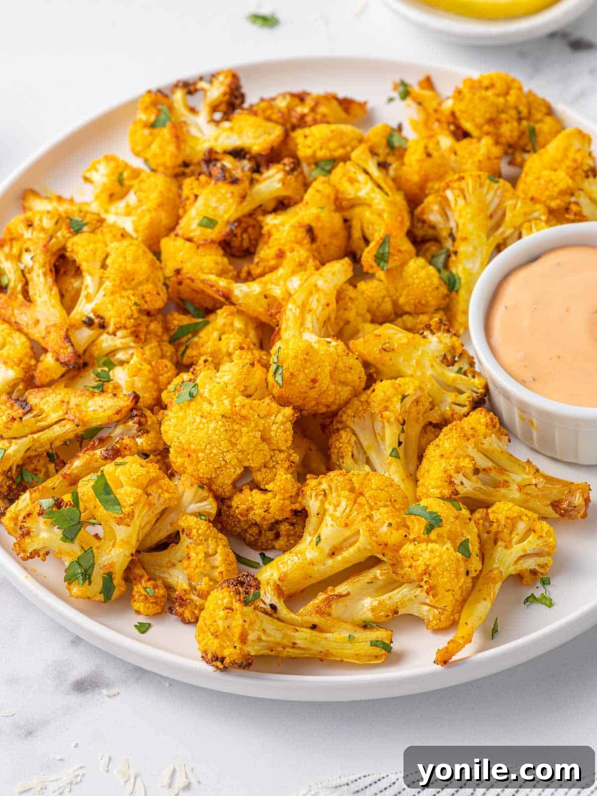 A beautifully arranged plate of roasted air fryer cauliflower bites, garnished with fresh herbs and accompanied by a small bowl of creamy dipping sauce.