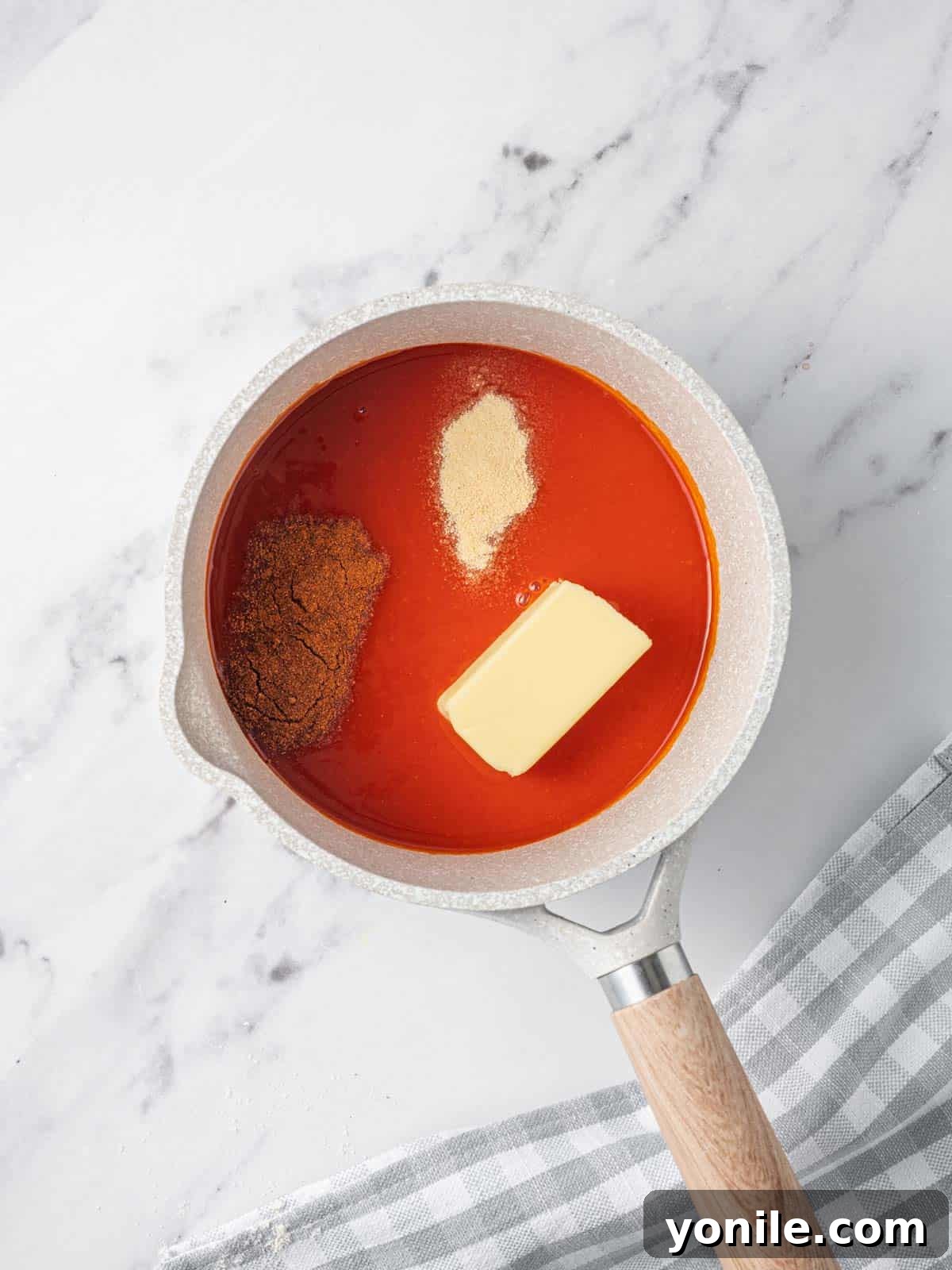 A saucepan filled with a simmering, rich red buffalo sauce, made from hot sauce, melted butter, and spices.