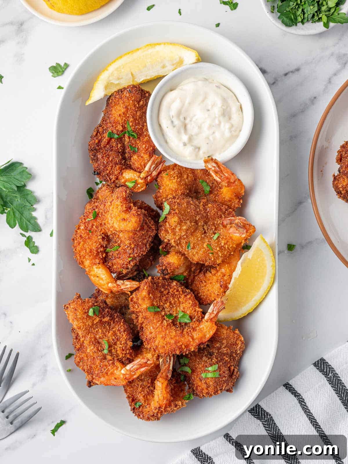 Golden-brown fried butterfly shrimp arranged artfully on a platter, garnished with vibrant lemon wedges and a side of creamy tartar sauce, ready to be served.