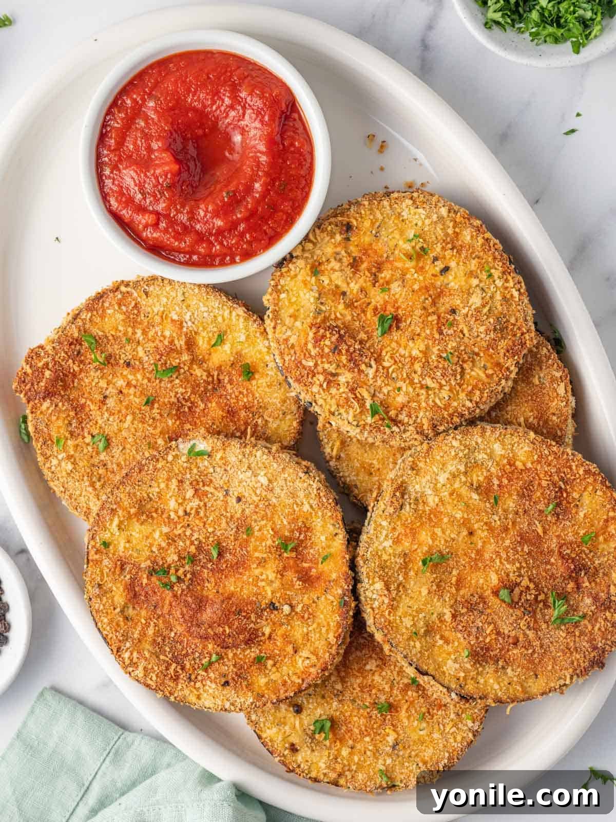 Golden Crispy Air-Fried Eggplant 2 A platter of golden, crispy air fried eggplant with a side of vibrant marinara sauce.