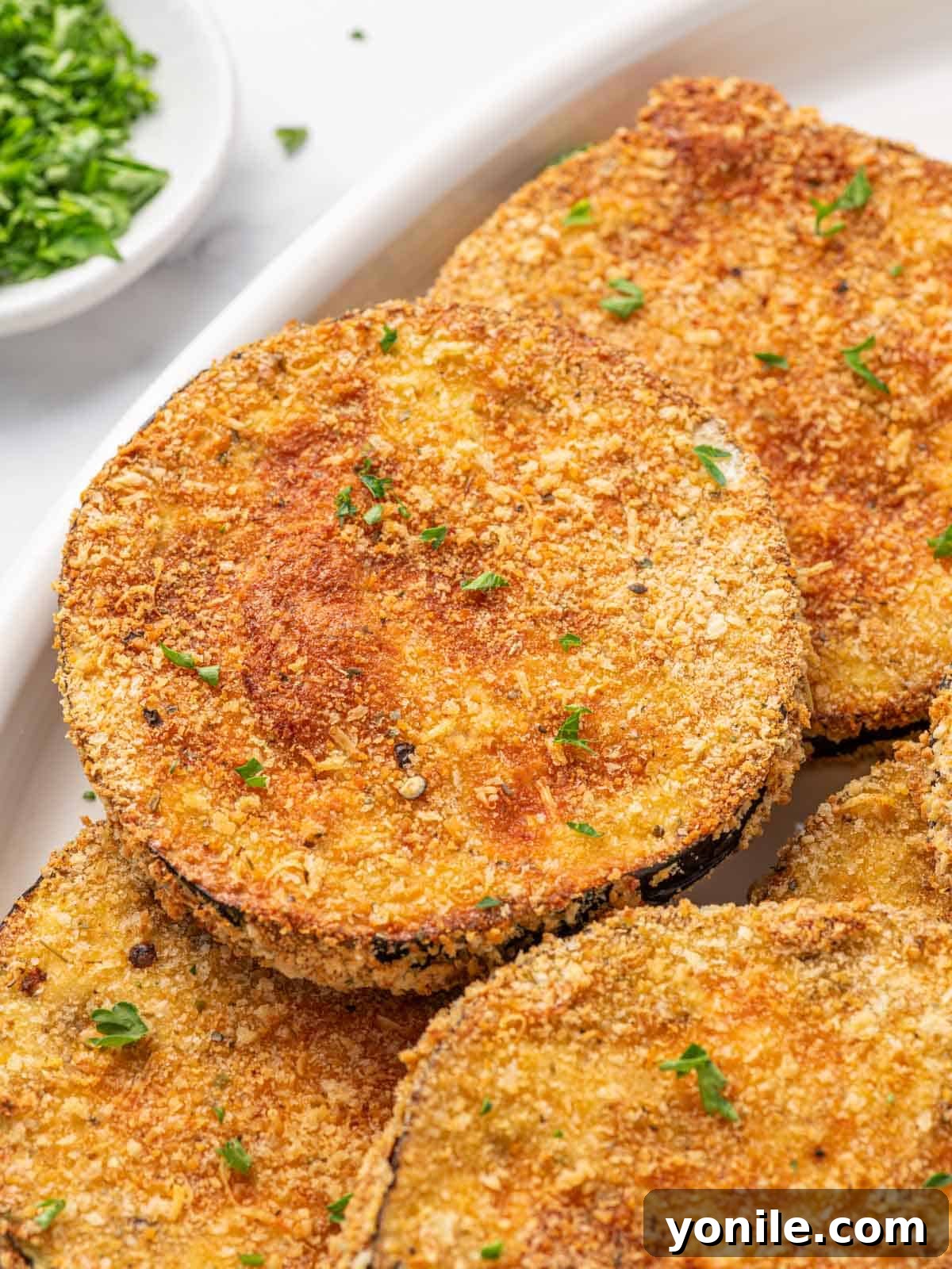 Golden Crispy Air-Fried Eggplant 8 Close-up of golden, crispy air fried eggplant garnished with fresh parsley on a white platter.