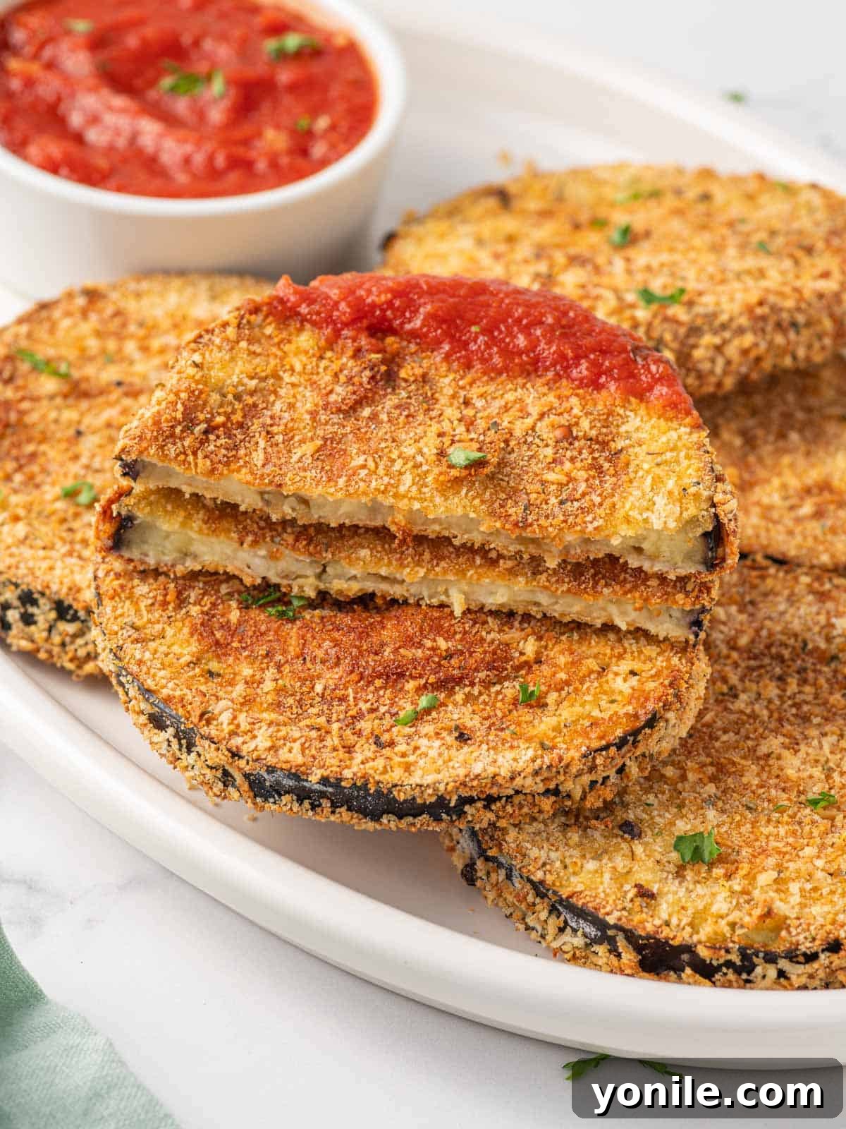 Golden Crispy Air-Fried Eggplant 9 A slice of breaded air fried eggplant being dipped into a bowl of marinara sauce.