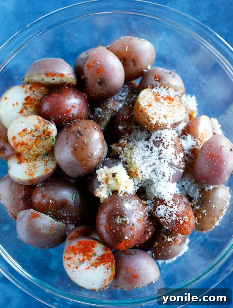 Red baby potatoes thoroughly tossed with aromatic herbs, savory spices, and grated Parmesan cheese in a mixing bowl, perfectly coated and ready for roasting.