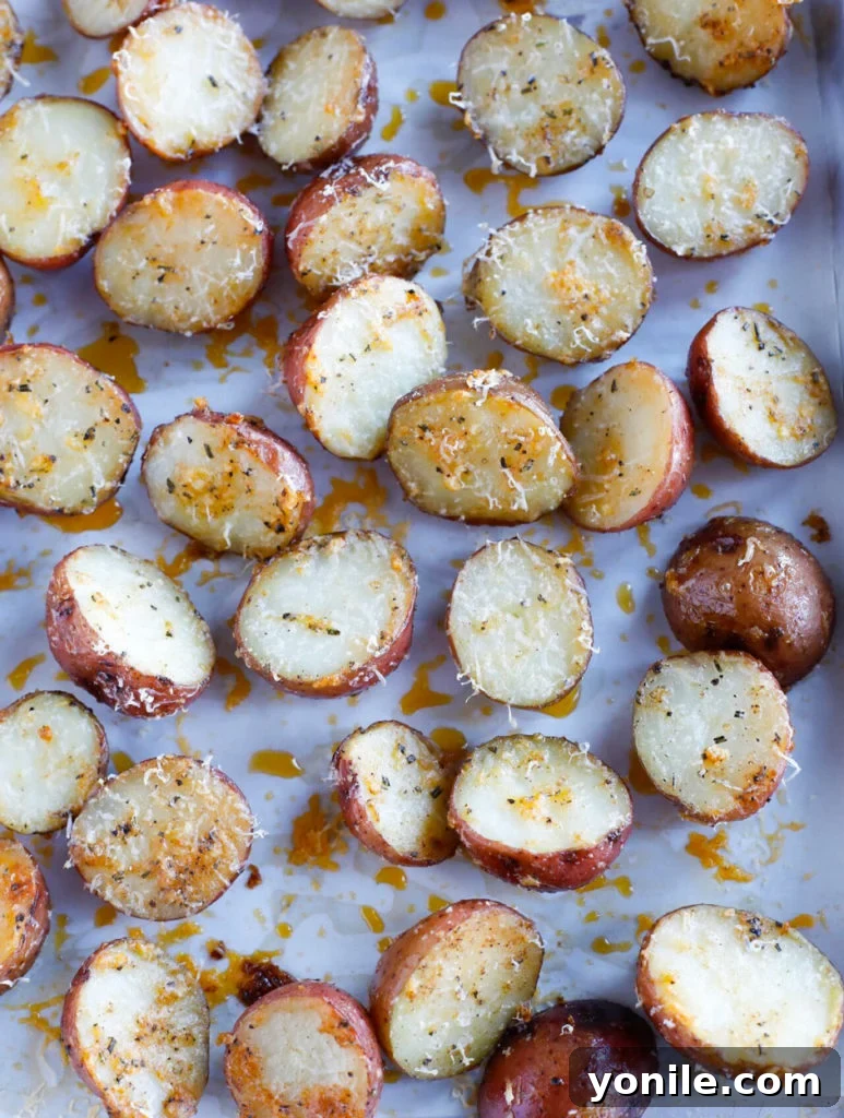 Coated potato halves meticulously arranged in a single layer on a parchment-lined baking sheet, evenly spaced and lightly sprinkled with extra Parmesan, ready for the oven.