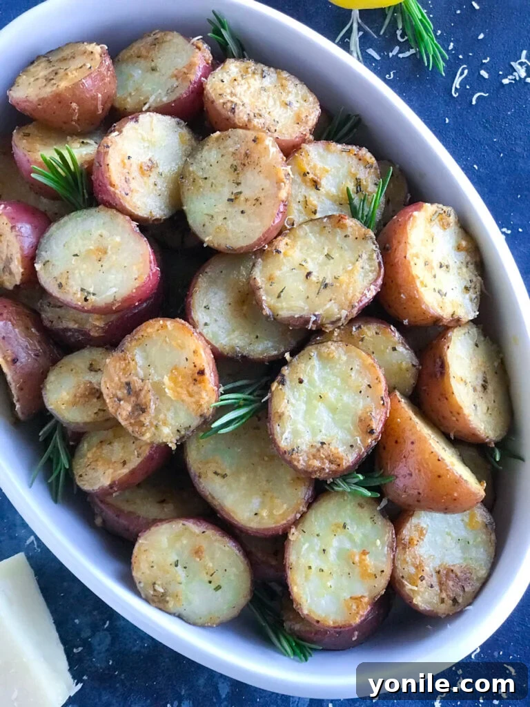 Beautifully arranged Oven Roasted Parmesan Herbed Potatoes served in a white bowl, generously garnished with fresh rosemary sprigs and parsley, ready to be enjoyed.