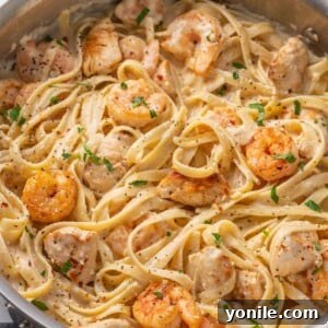 A skillet with pasta, chicken and shrimp topped with alfredo sauce.