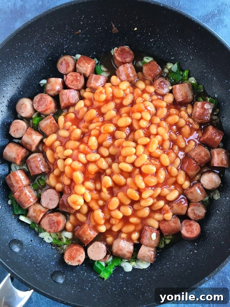 A beautifully plated bowl of Baked Beans and Sausage Egg Brunch, accompanied by toasted pita bread and a fresh avocado slice.