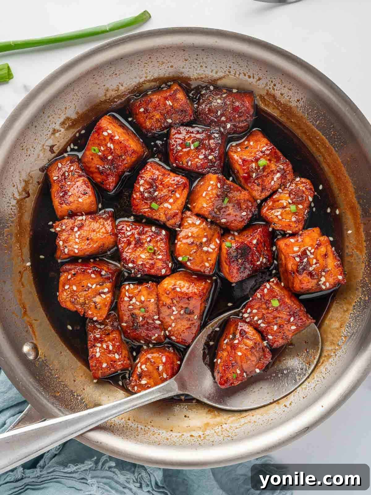 Glazed Honey Garlic Salmon Bites 7 A stirring spoon mixing salmon pieces with the thick honey garlic soy sauce in a skillet, showcasing the glaze.