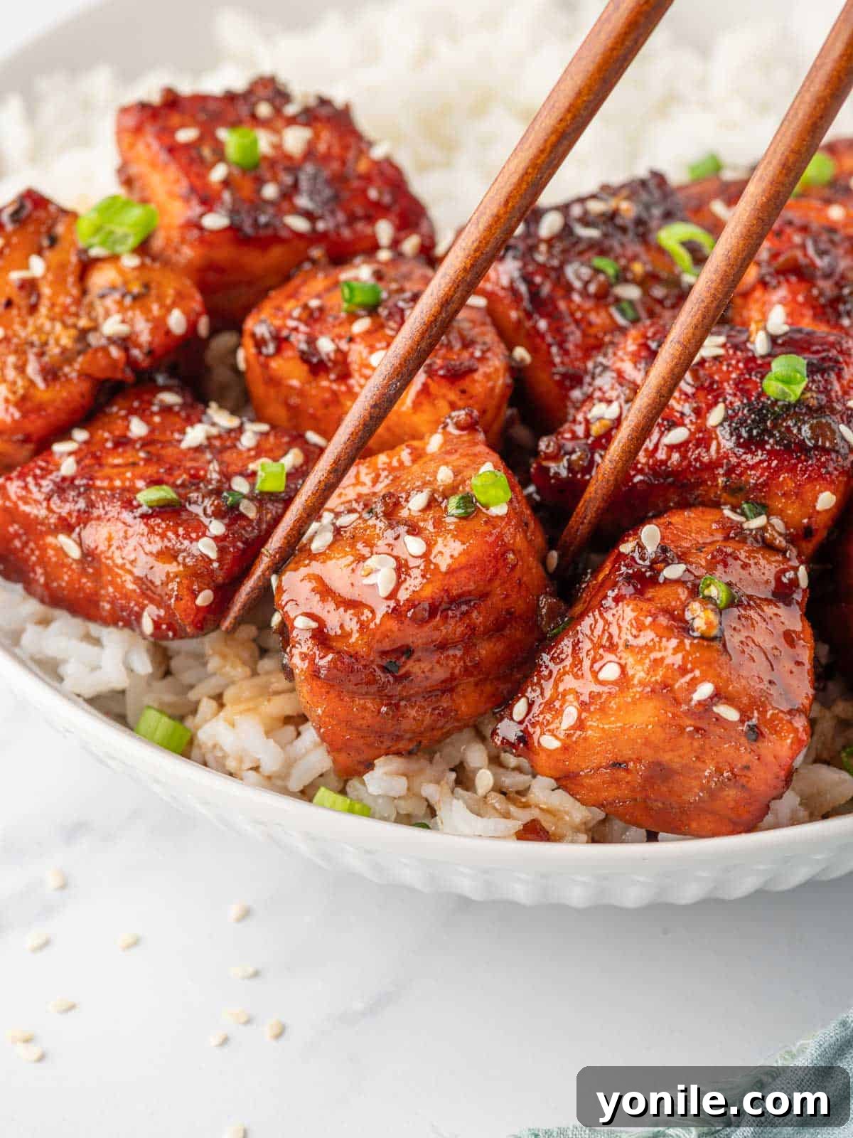 Glazed Honey Garlic Salmon Bites 9 Chopsticks delicately picking up a piece of honey garlic salmon from a serving dish, highlighting the perfect bite-sized portion.