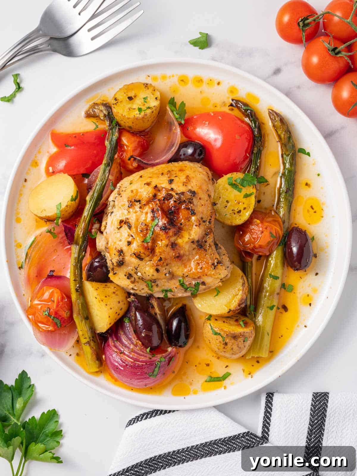 A plate of golden-brown Mediterranean chicken thighs surrounded by roasted vegetables like potatoes, bell peppers, asparagus, and cherry tomatoes, garnished with fresh parsley and Kalamata olives.