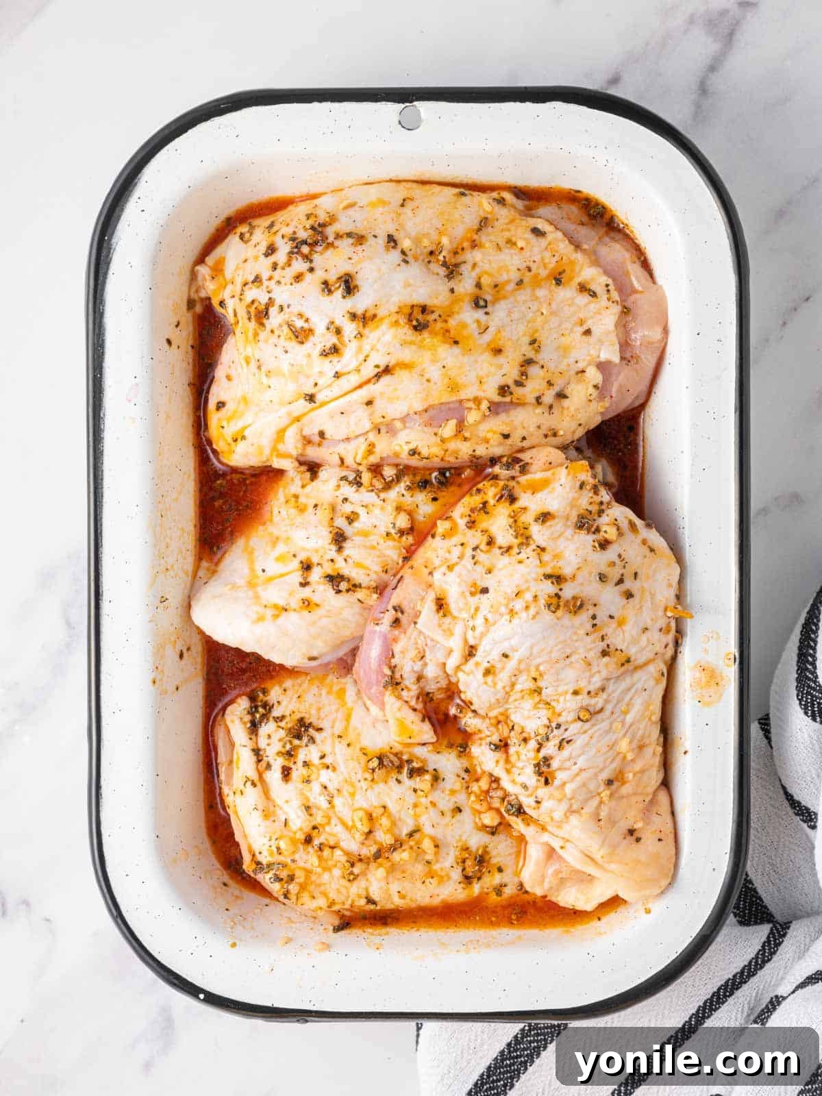 Raw chicken thighs marinating in a glass dish, covered with a bright, herb-infused Mediterranean marinade.