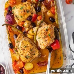 A spoon picks up a juicy chicken thigh from a Mediterranean bake.