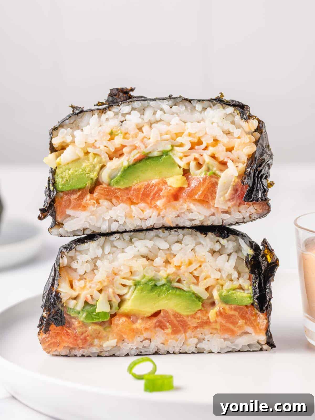 Two halves of a vibrant nori wrap sushi burger stacked on top of each other, showcasing layers of salmon, crab, and avocado.