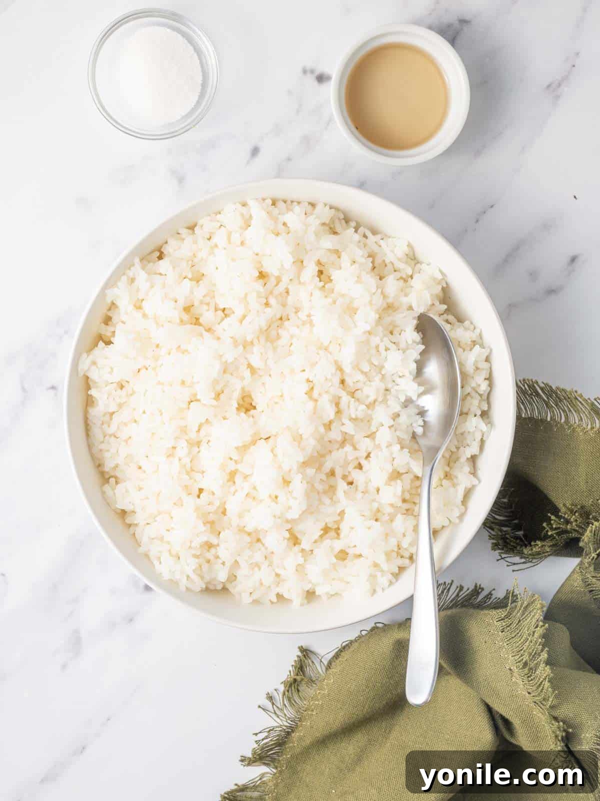 A spoon gently stirs a bowl of warm sushi rice with added sugar and rice vinegar, preparing it for the sushi burger buns.