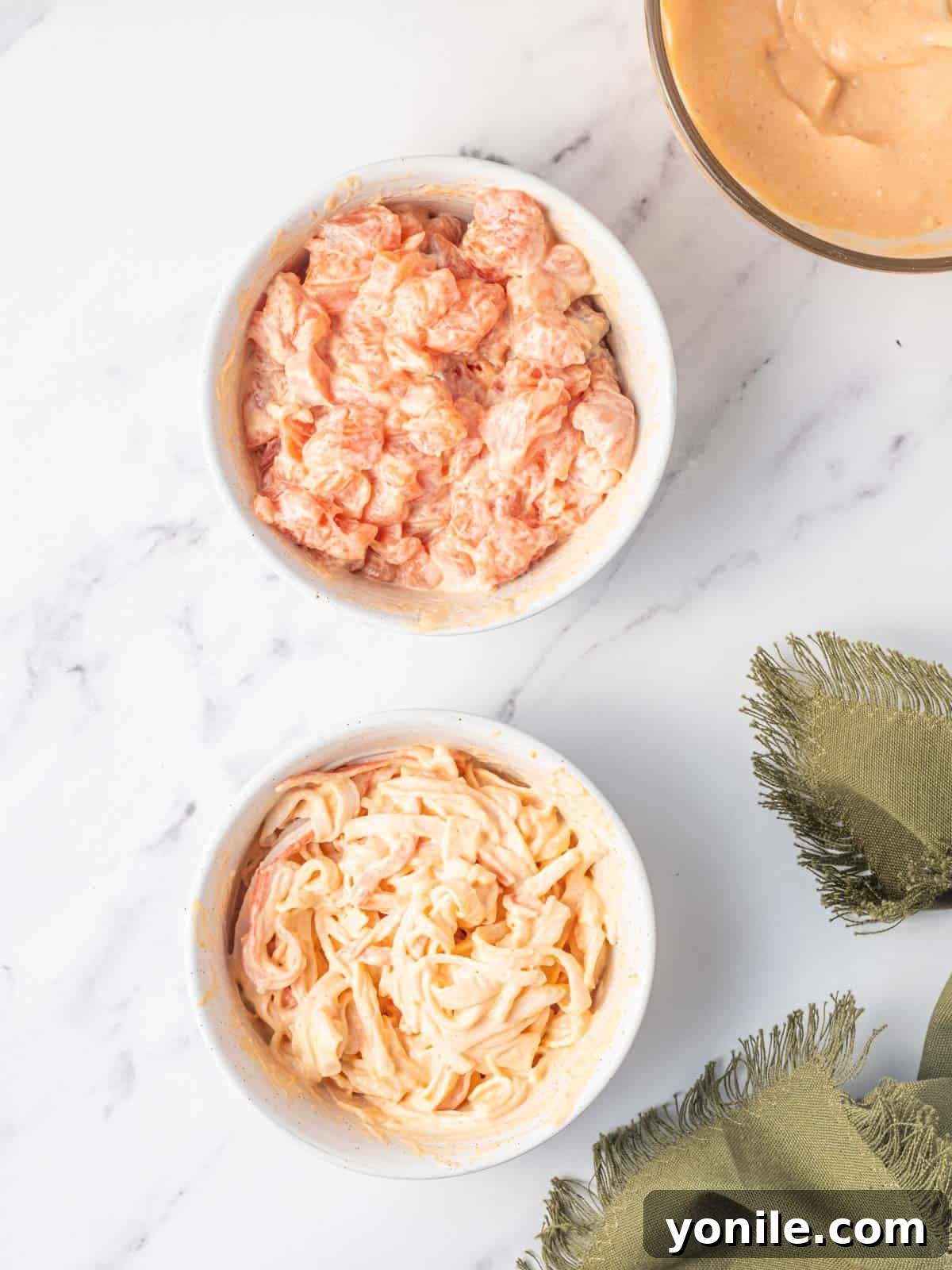 Separate bowls containing seasoned salmon and imitation crab mixtures, ready to be layered into the sushi rice buns for the burger.