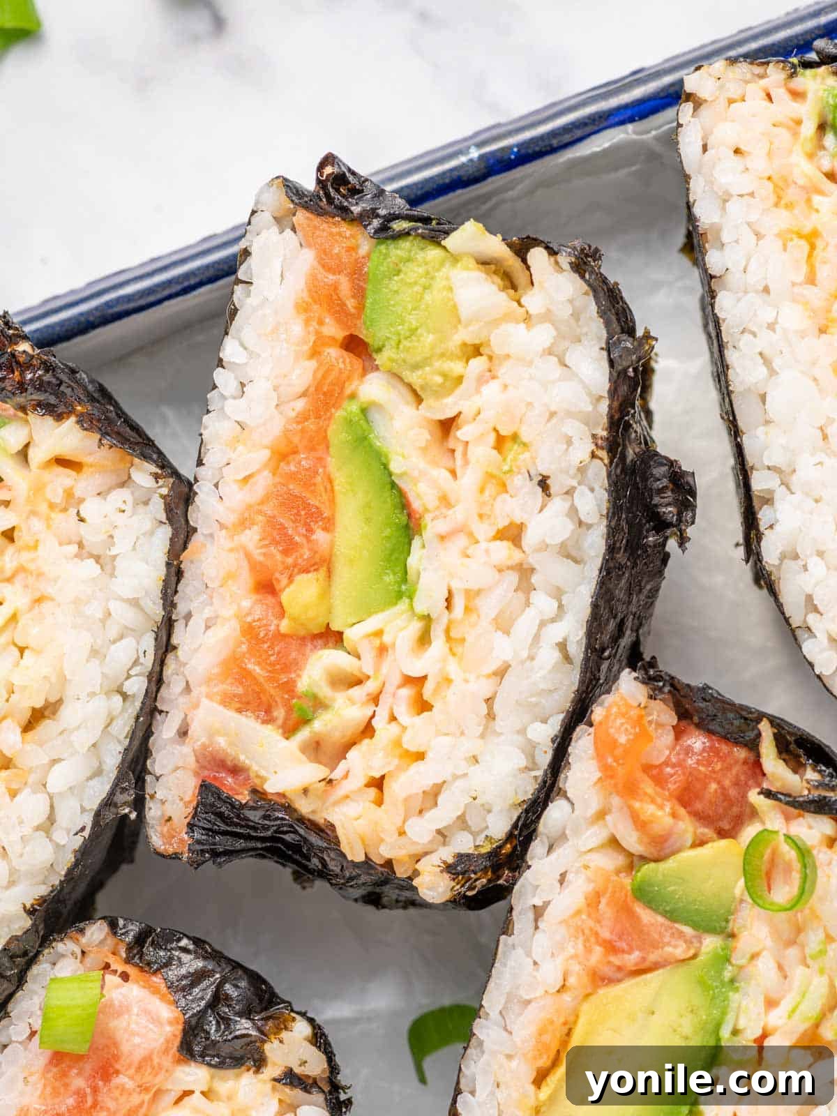 A beautifully presented sushi burger, sliced in half, showcasing its vibrant layers of ingredients on a stylish serving tray.