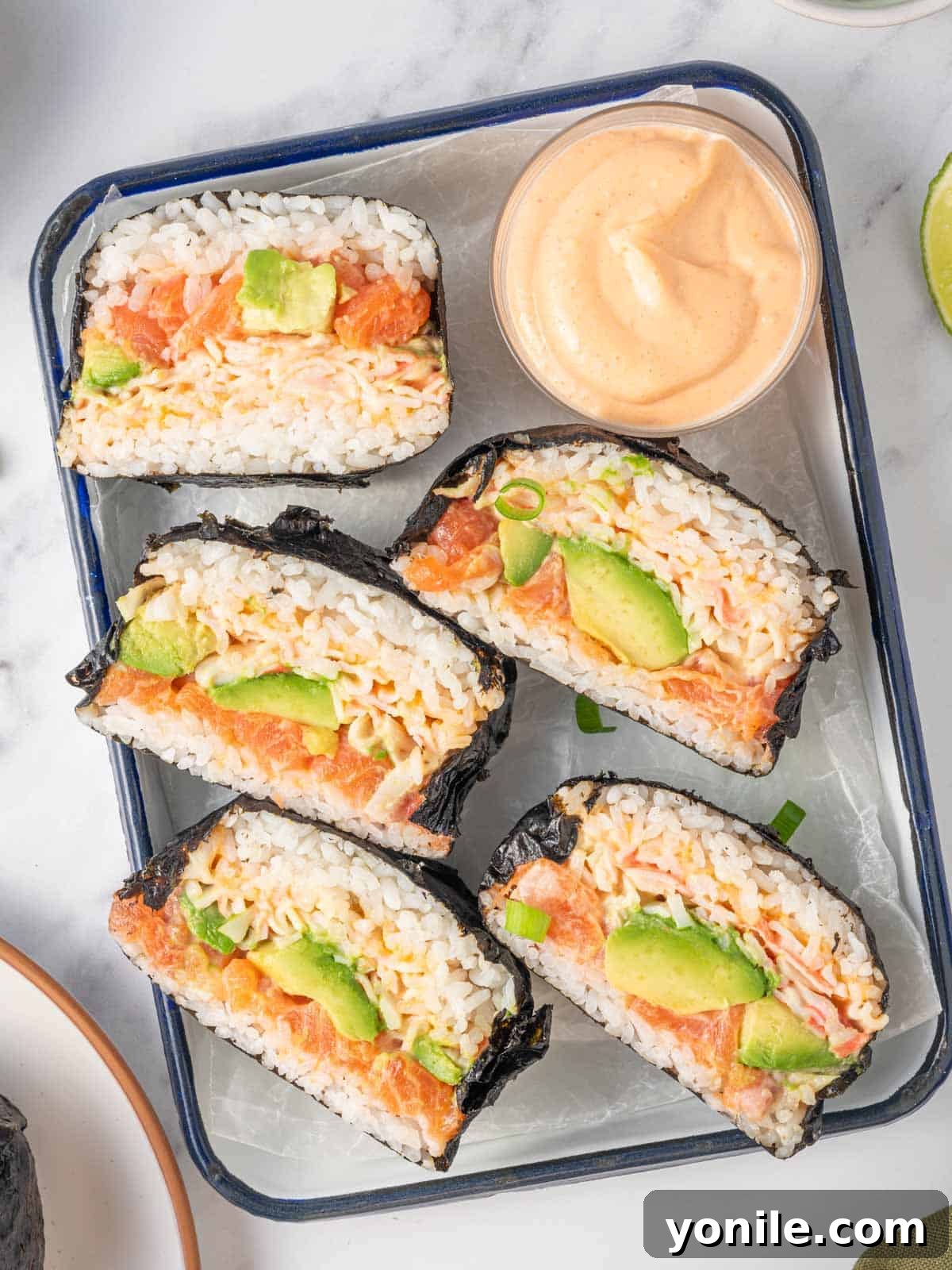 A tray filled with multiple rice bun sushi burgers, each neatly sliced in half to display their vibrant, layered fillings.