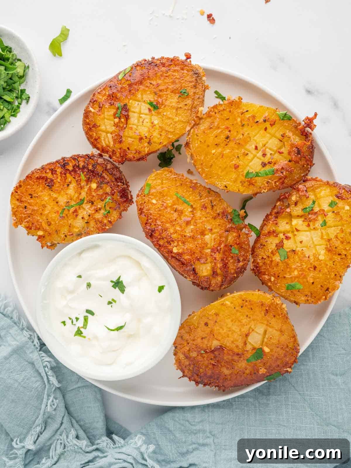 A plate of crispy parmesan potatoes with a side of sour cream.