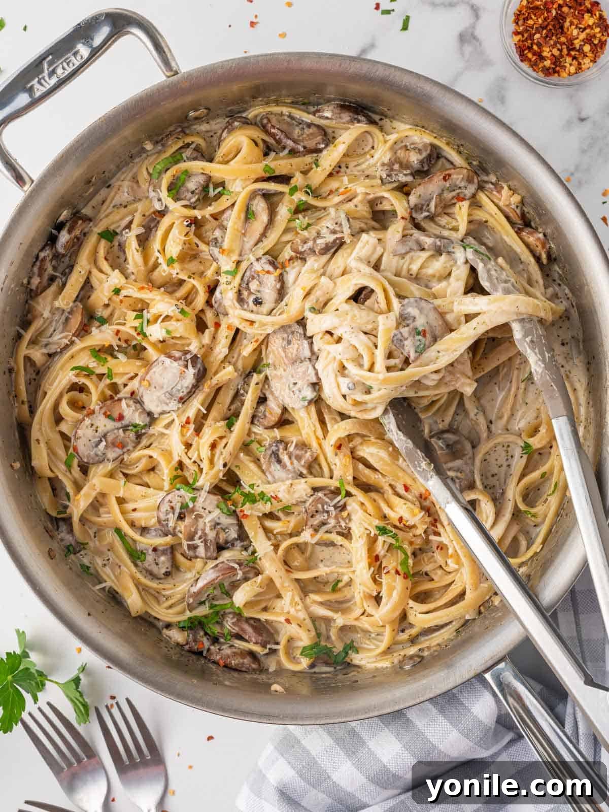 Mushroom pasta is being stirred in a skillet with tongs, showing its creamy texture.