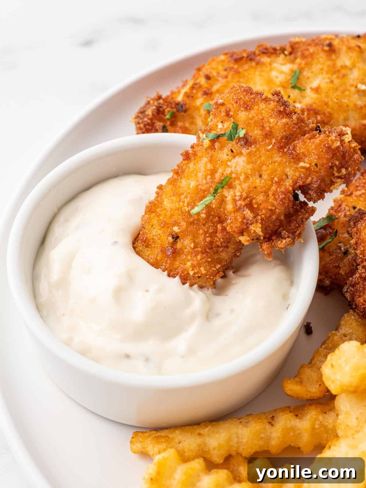 Crispy Gluten Free Fish and Chips 7 Panko crusted cod is dipped into tarter sauce, highlighting the crispy texture.