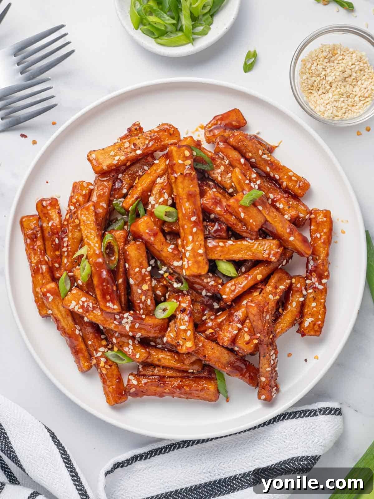 Sweet and Spicy Honey Chilli Potatoes 2 A plate of golden-brown honey chilli fries, generously coated in a glossy, vibrant red sauce and garnished with sesame seeds and chopped green onions.