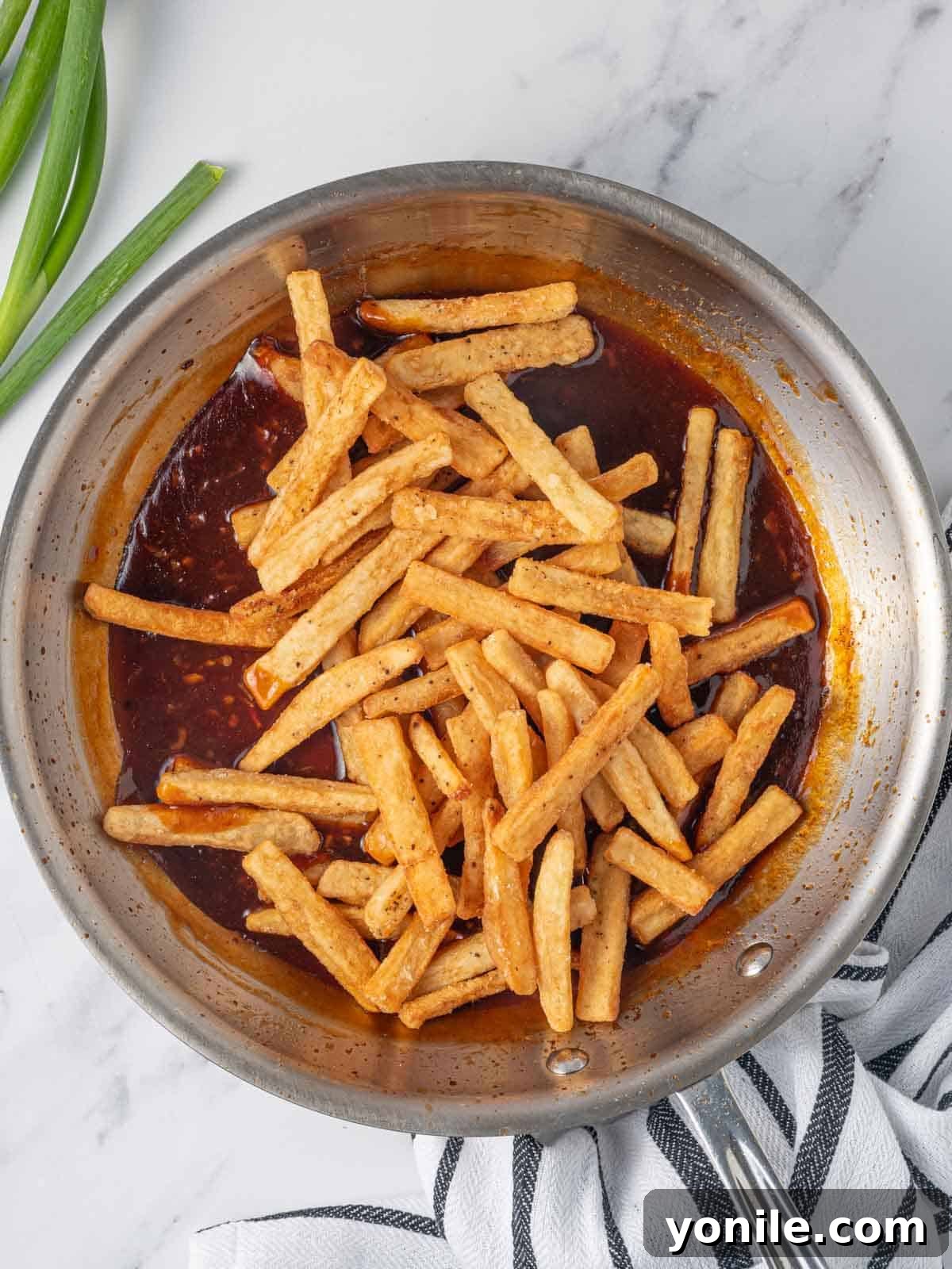 Sweet and Spicy Honey Chilli Potatoes 7 Crispy fried potato fries being tossed vigorously in a pan filled with the vibrant red honey chilli sauce.