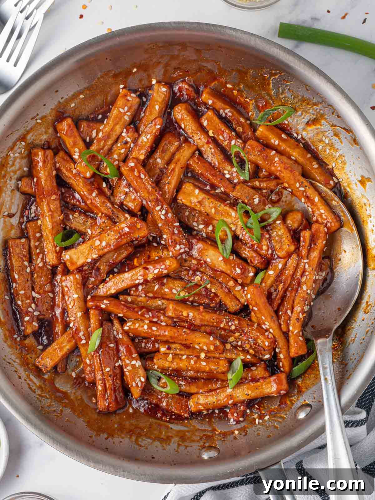 Sweet and Spicy Honey Chilli Potatoes 8 A serving of honey chilli potatoes in a rustic skillet with a spoon, garnished with sesame seeds and green onions, ready to be enjoyed.