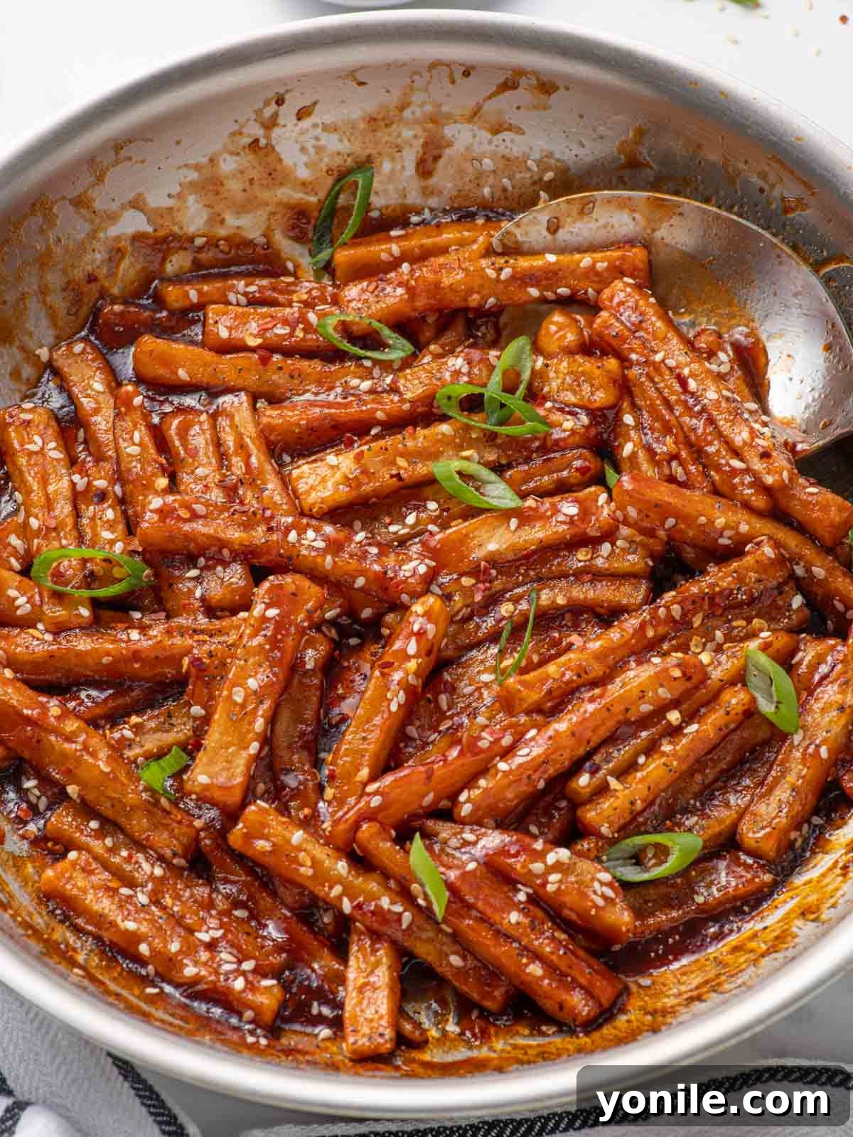 Sweet and Spicy Honey Chilli Potatoes 9 A spoon gently coating crispy potato fries with the vibrant red honey chilli sauce in a pan.