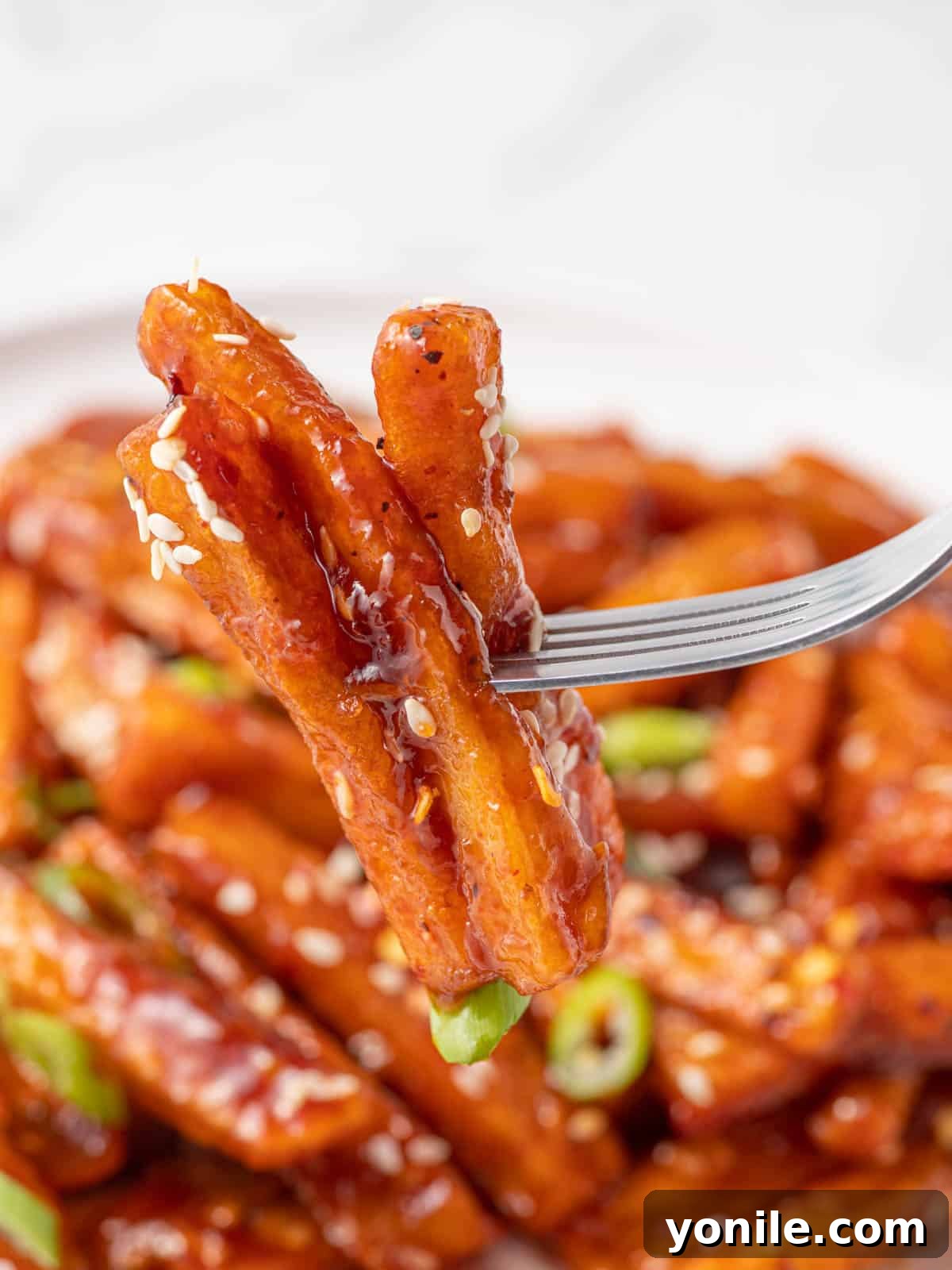 Sweet and Spicy Honey Chilli Potatoes 10 A close-up of a fork picking up a serving of sticky sweet chilli fries, coated in sauce and garnished with sesame seeds and green onions.