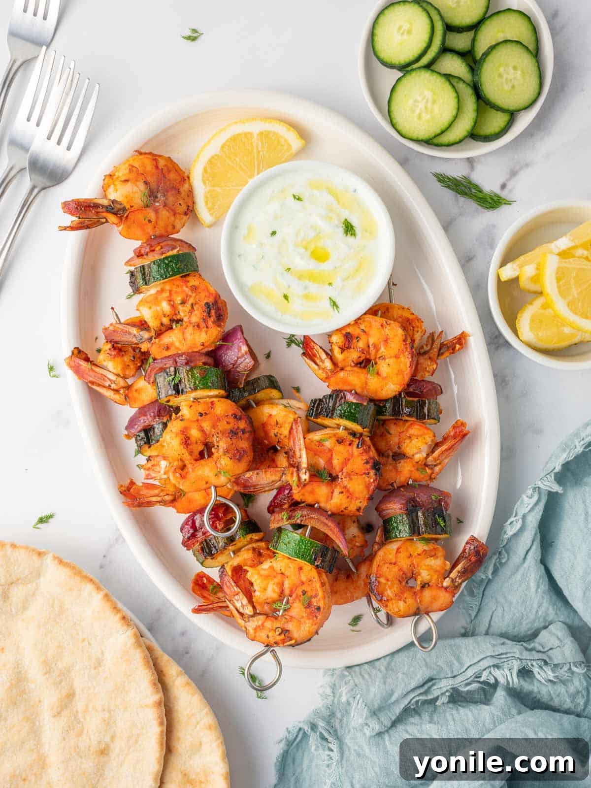 A platter of vibrant grilled shrimp skewers with zucchini and red onions, garnished with fresh herbs and lemon wedges, ready to be served.