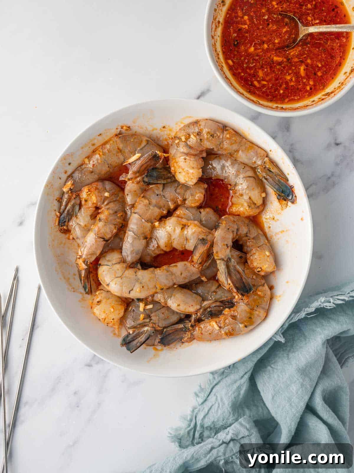 A glass bowl filled with jumbo shrimp, glistening with a vibrant orange-yellow marinade, being tossed to ensure even coating.