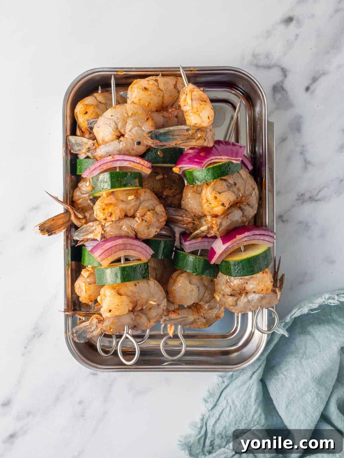 Several shrimp skewers, expertly threaded with plump shrimp, round zucchini slices, and vibrant red onion cubes, arranged neatly on a baking sheet, ready for the oven.