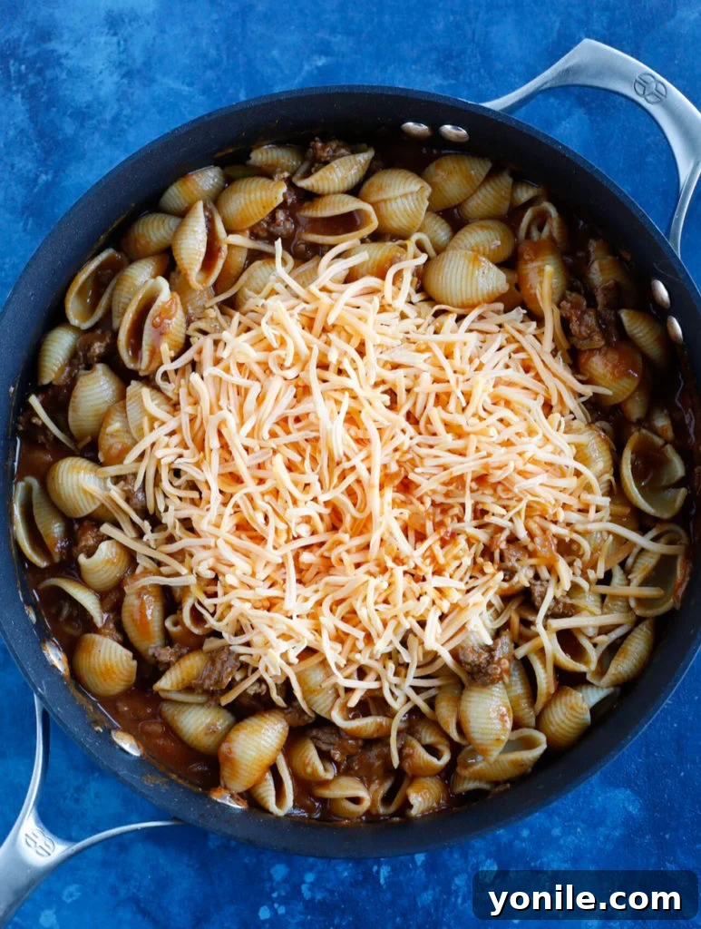 Close-up shot of shredded cheese melting on top of hot Beef Taco Pasta in a skillet.