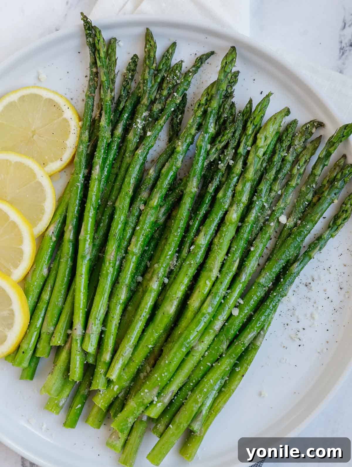 Crispy air fried asparagus on a plate, garnished with lemon wedges.