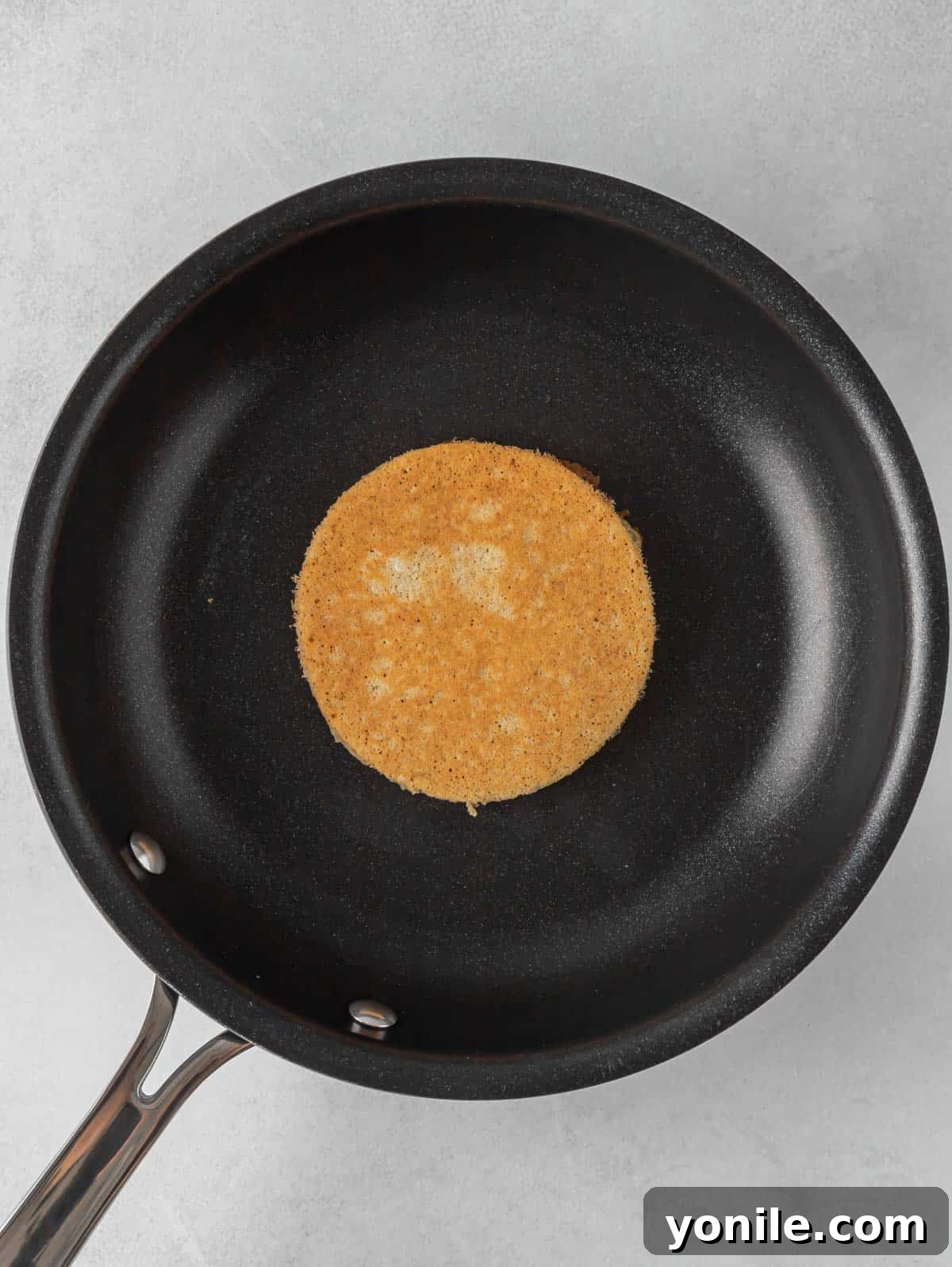 Power-Packed Banana Protein Pancakes 6 A non-stick skillet on medium heat, with several small banana protein pancakes cooking, showing bubbles forming on the surface as they become golden brown.