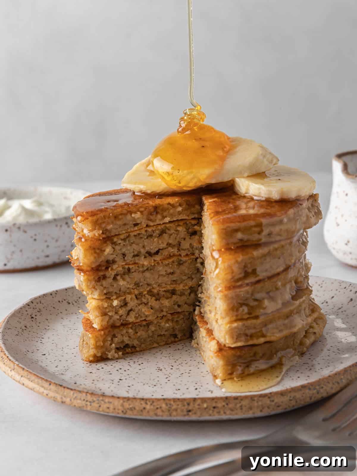 Power-Packed Banana Protein Pancakes 7 A close-up shot of rich maple syrup being drizzled over a stack of warm, golden banana protein pancakes, highlighting their fluffy texture.