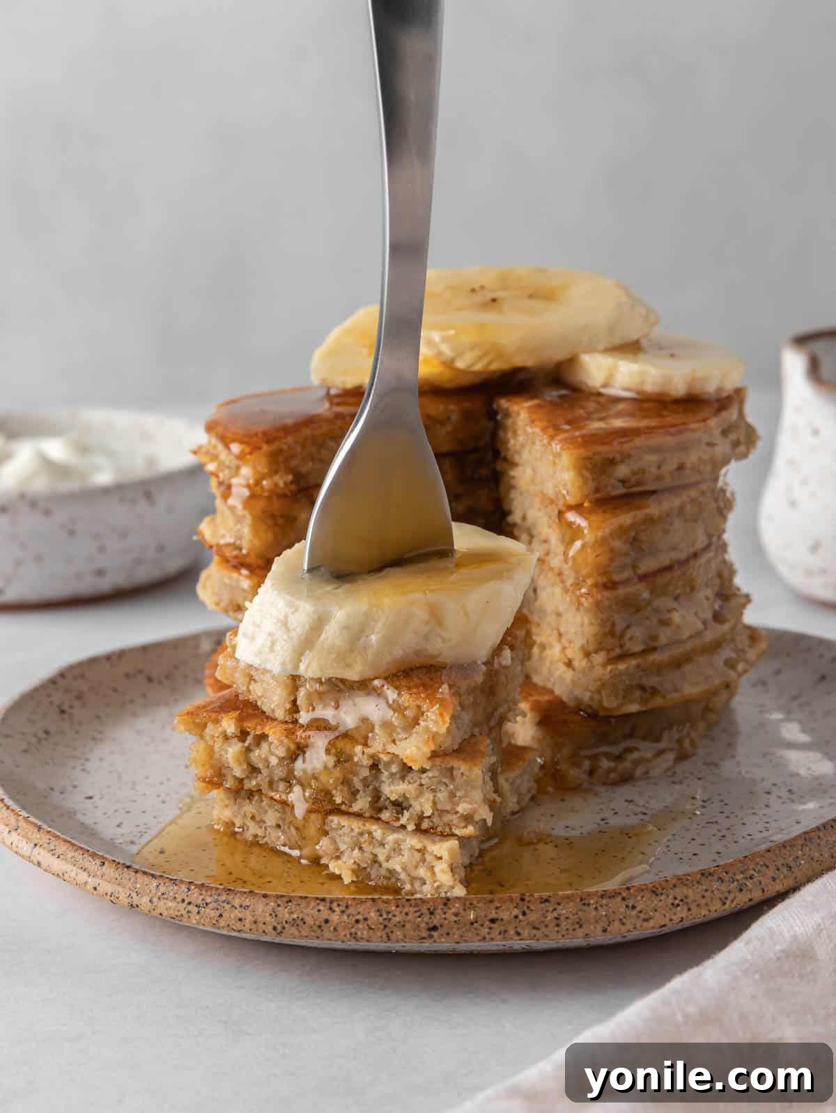 Power-Packed Banana Protein Pancakes 8 A hand holding a fork, picking up a fluffy bite of banana protein pancake, revealing its soft interior and golden crust.