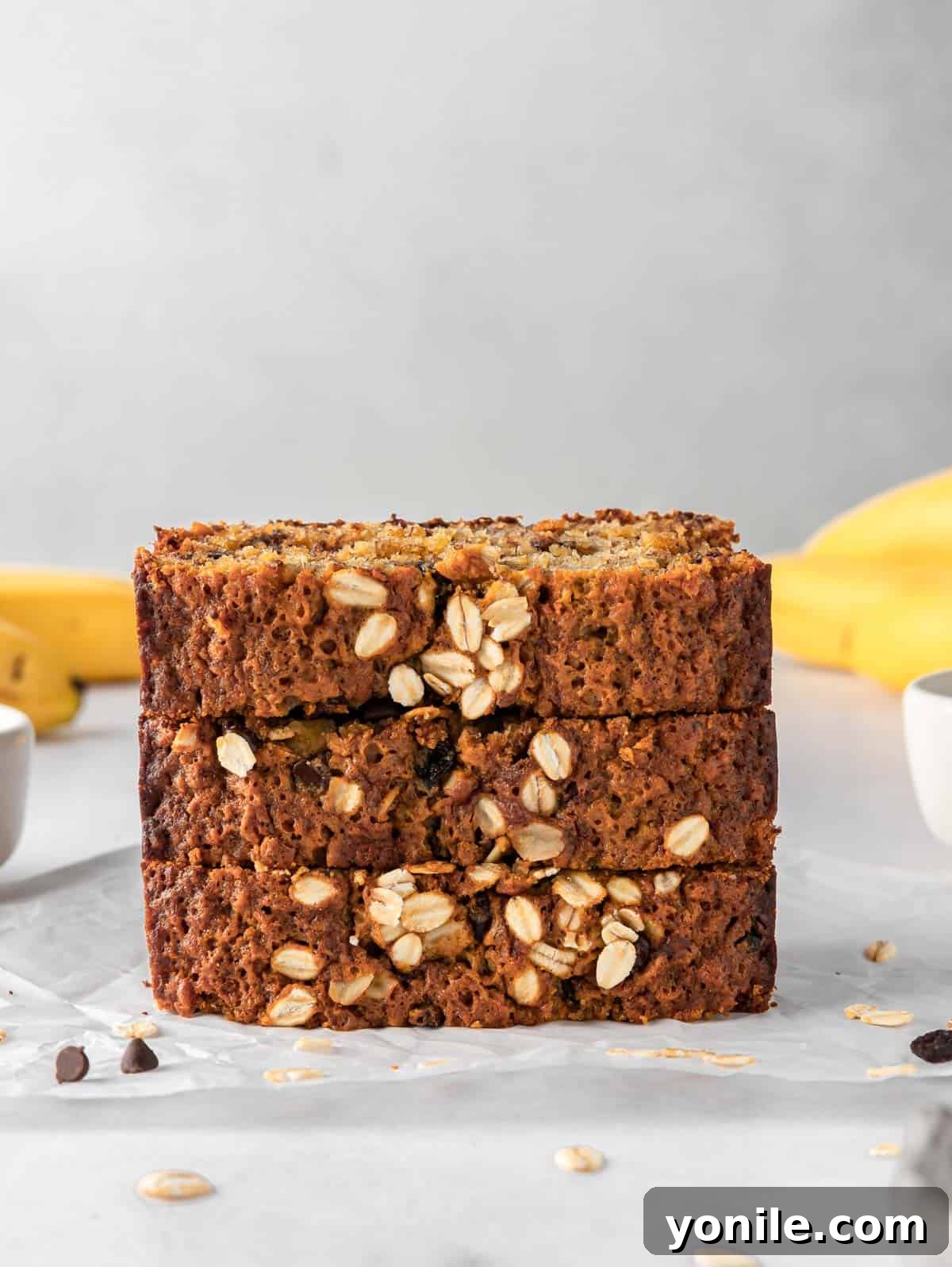 Wholesome Oat Banana Loaf 7 A stack of golden-brown banana bread slices, with fresh bananas in the background, ready to be enjoyed.