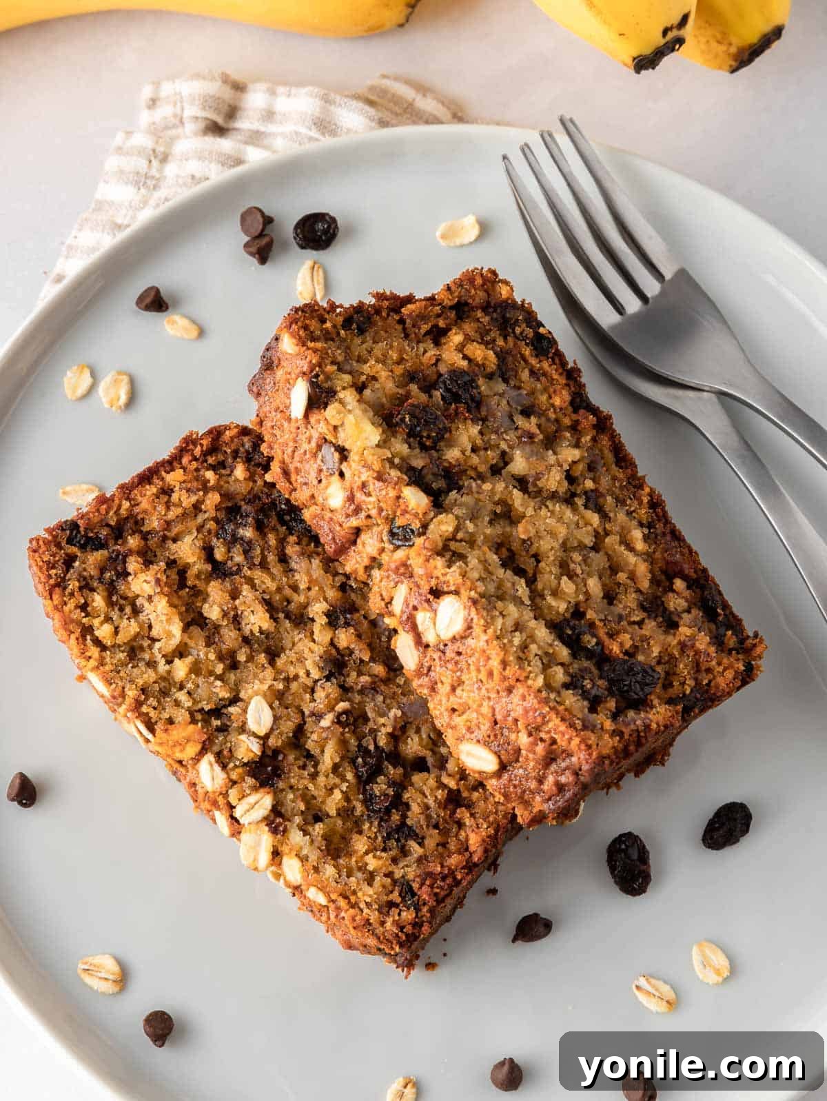 Wholesome Oat Banana Loaf 8 Two generous slices of healthy banana bread with oats on a white plate, accompanied by two forks, ready to be enjoyed.