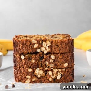 Wholesome Oat Banana Loaf 9 A stack of banana bread slices with bananas in the background.