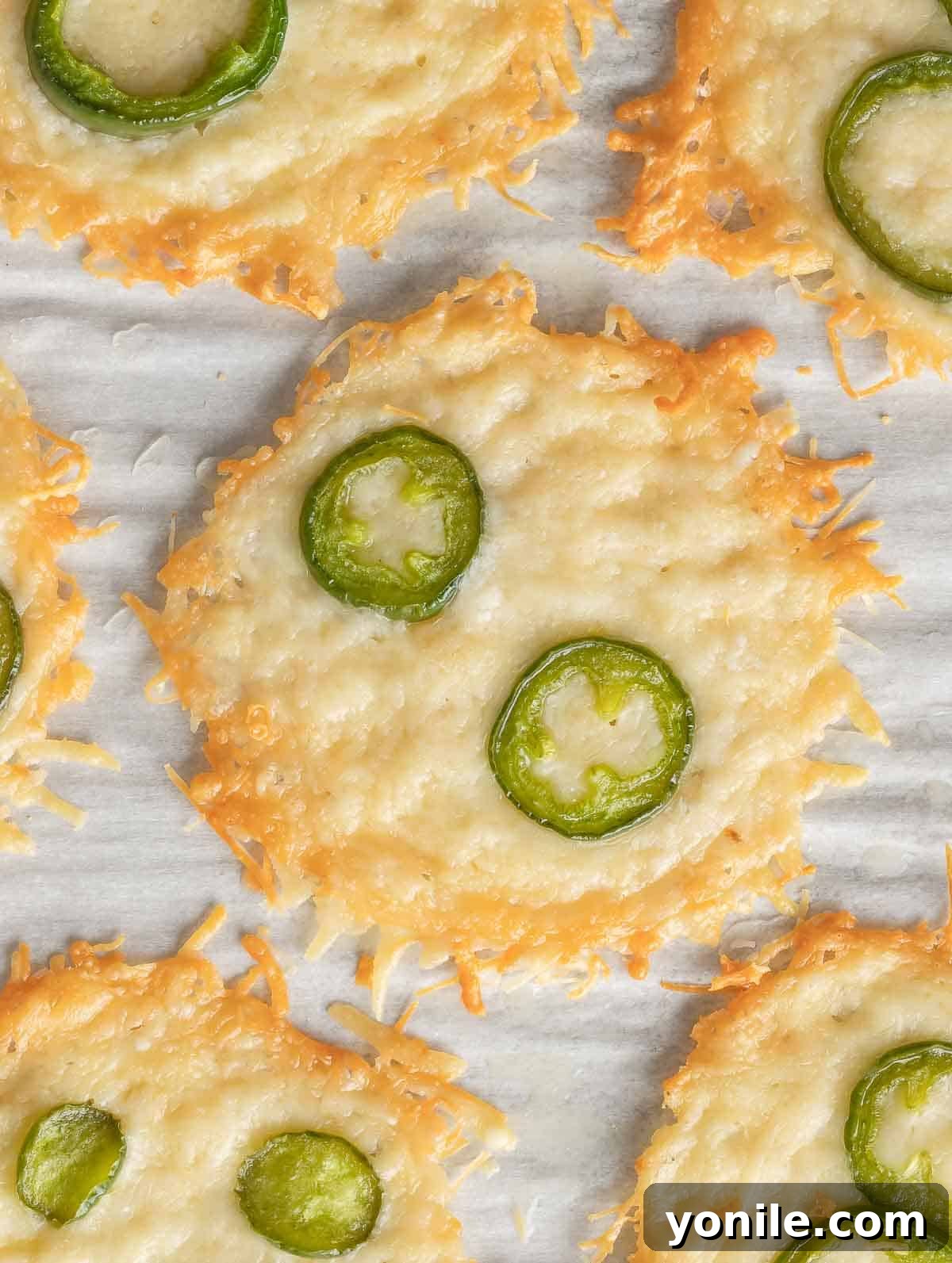 Crispy Parmesan Bites 7 Parmesan chips topped with slices of vibrant green jalapeno, arranged on a baking sheet.