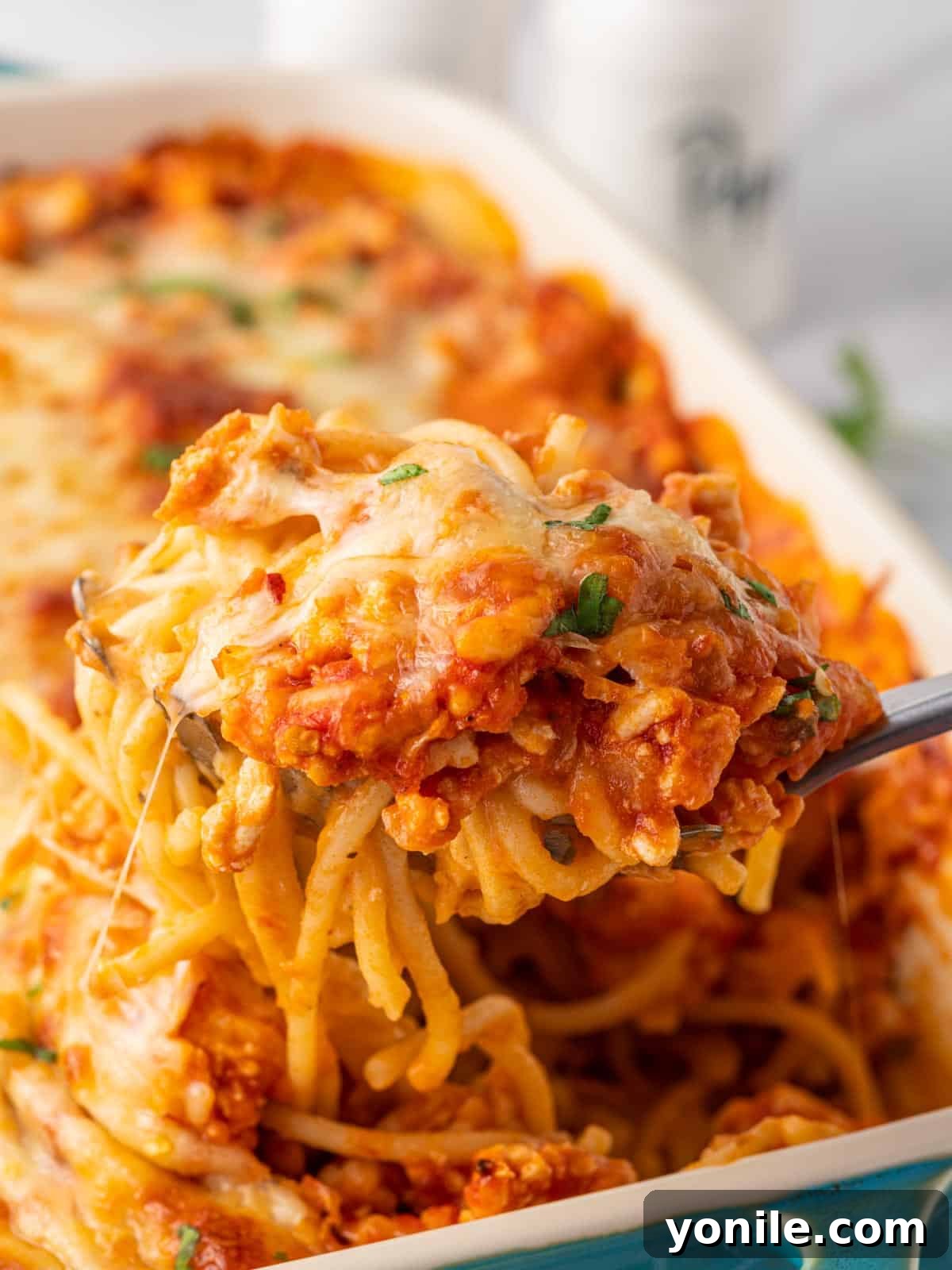 A spoon serves a helping of million dollar spaghetti from a casserole dish.