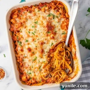 A spoon rests in a casserole dish of million dollar spaghetti, showing the layers of sauce and cheese.