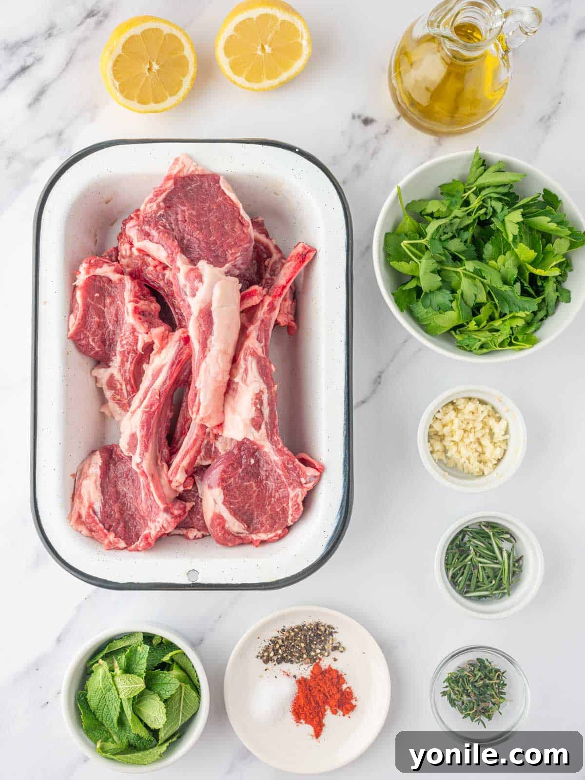 A flat lay of fresh ingredients laid out for making Mediterranean lamb chops, including lamb chops, fresh herbs, lemon, garlic, and olive oil.