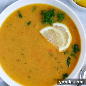 Lebanese lentil soup served in a white bowl and garnished with lemon wedges and parsley