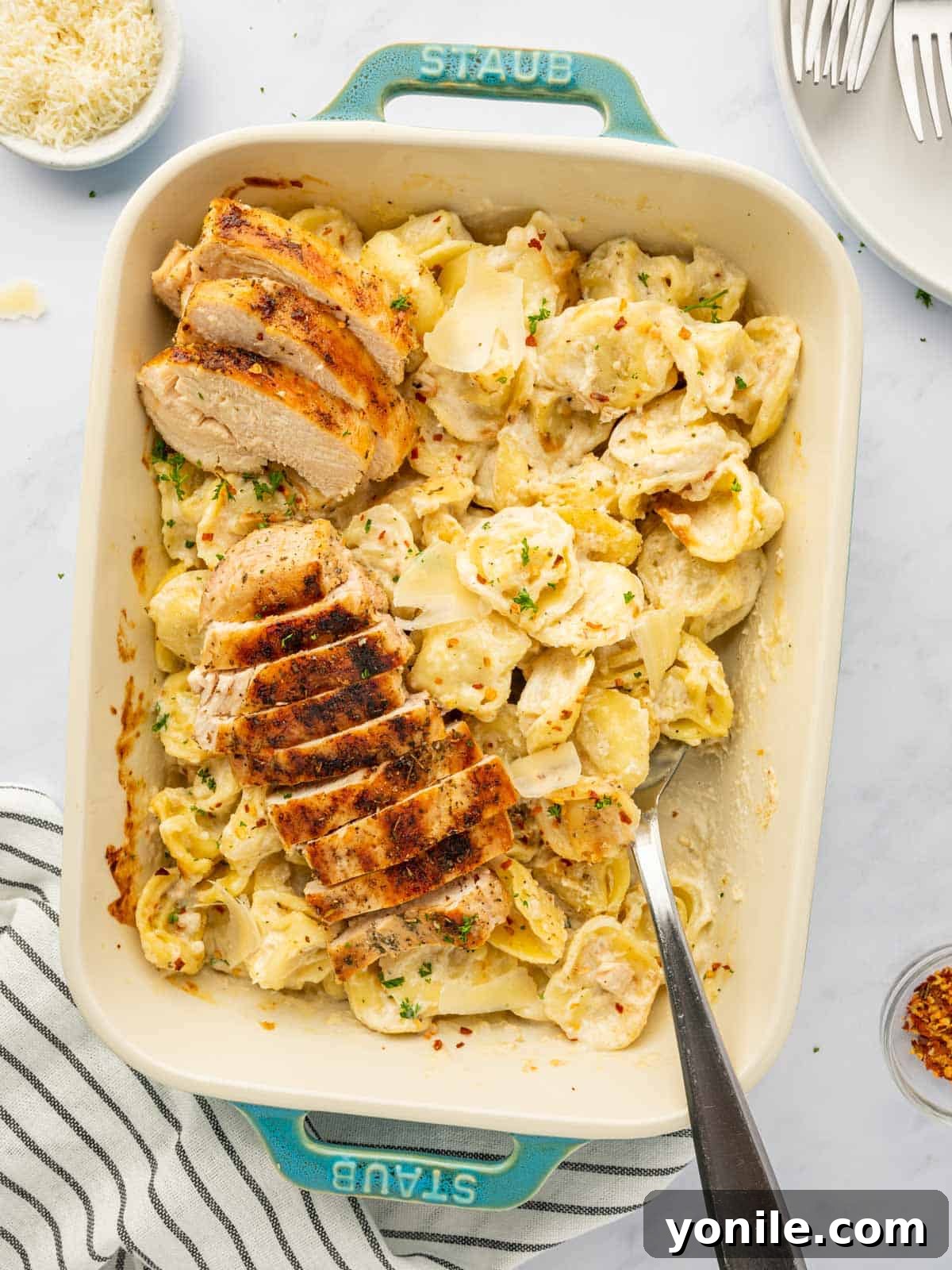 Velvety Chicken Tortellini Alfredo 8 A hand dishing out a spoonful of creamy alfredo tortellini from a baking dish.