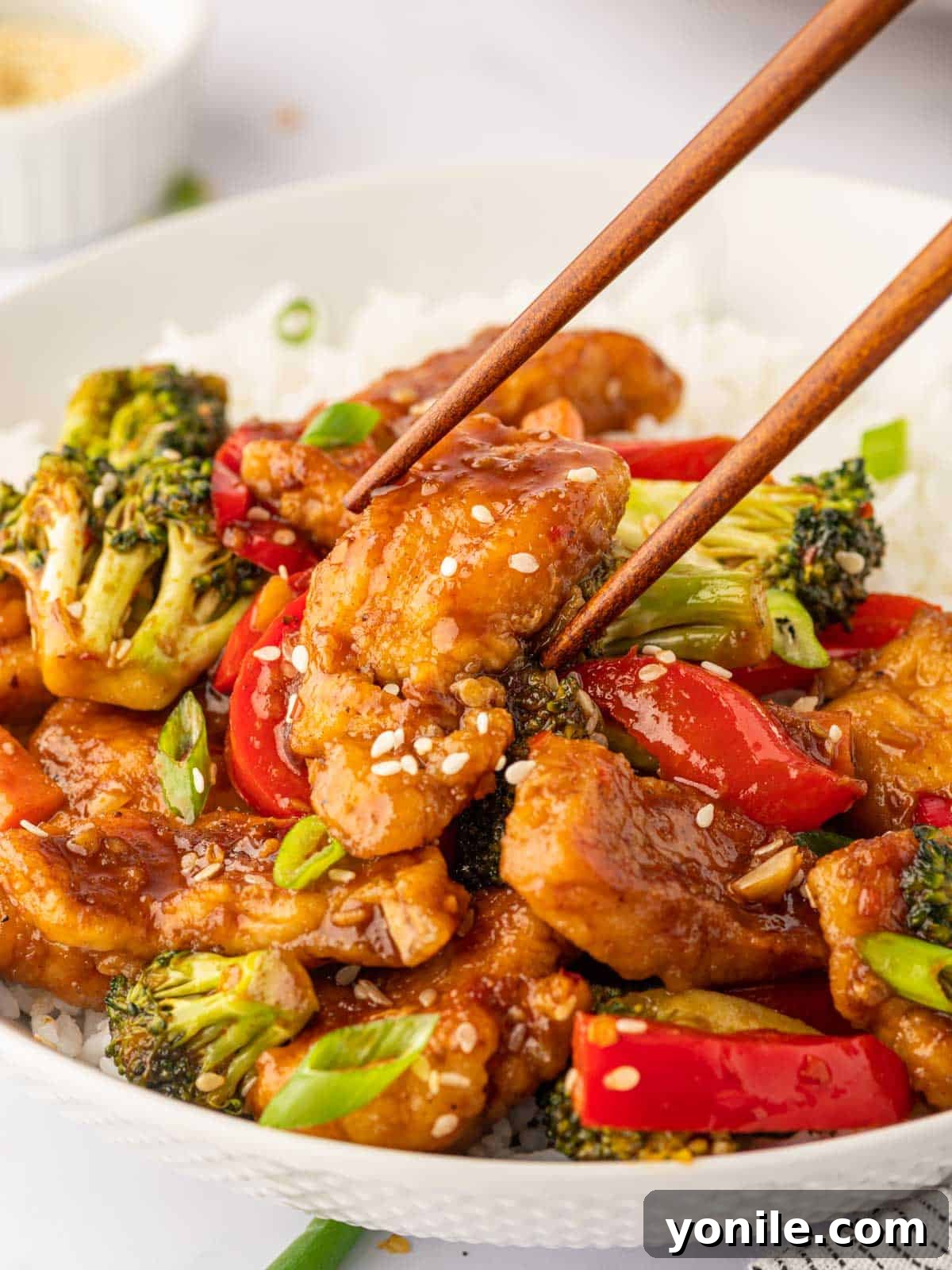 Fiery Hunan Chicken 9 Chopsticks picking up a piece of delicious Hunan style chicken, ready to be enjoyed with its rich sauce.